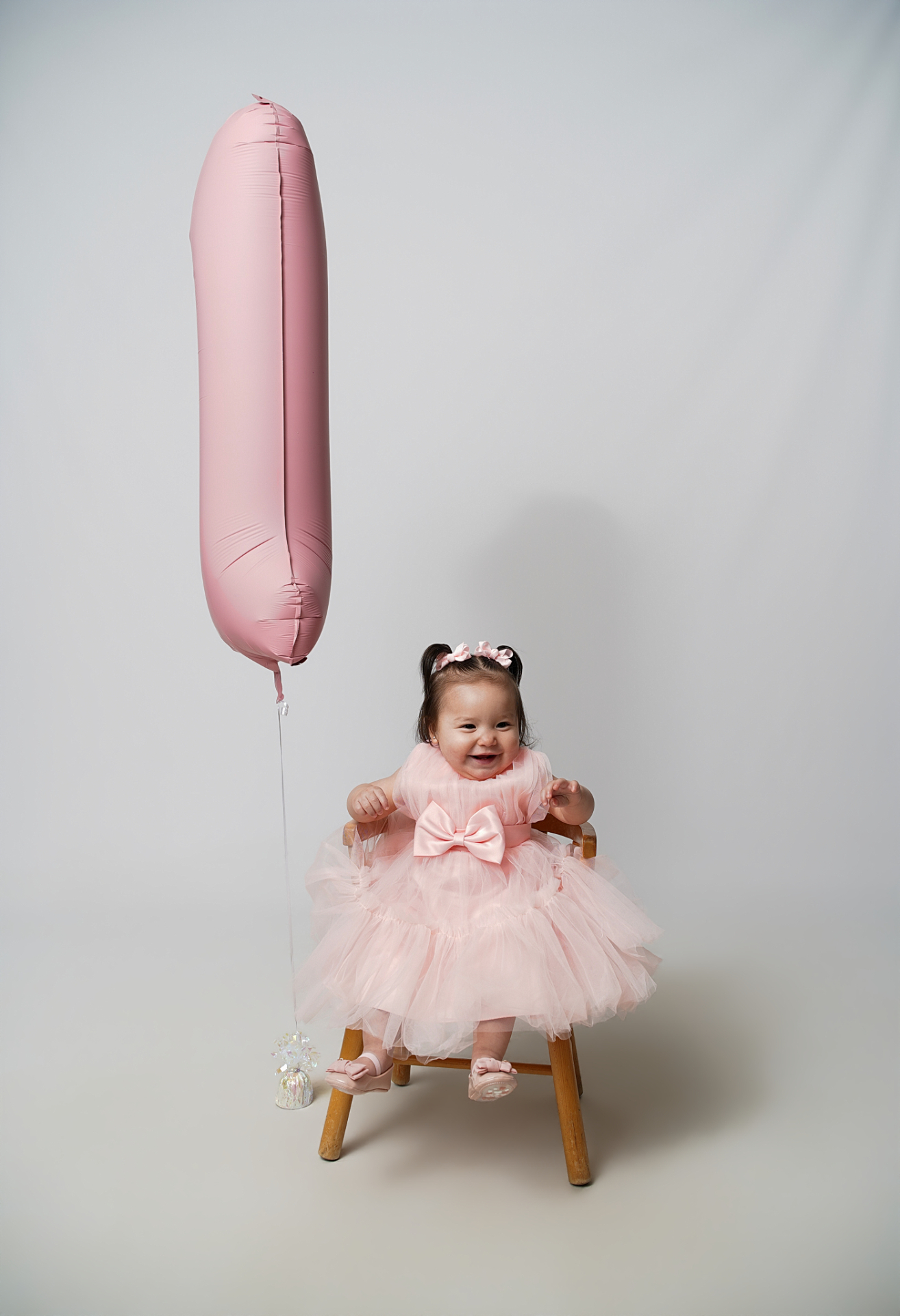 Joyful first birthday smile on wooden stool with pink balloon