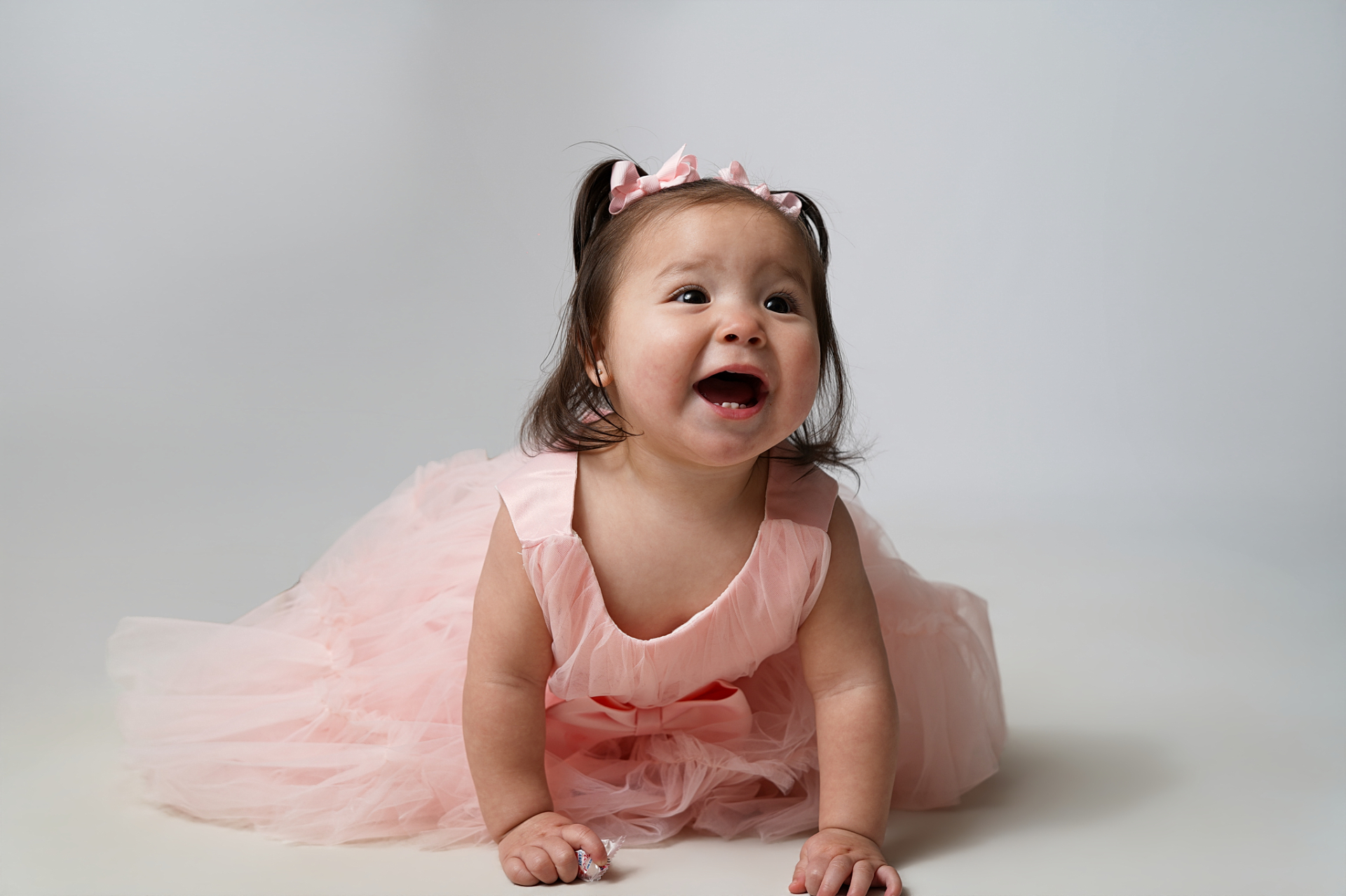 Playful first birthday studio portrait with pink bows