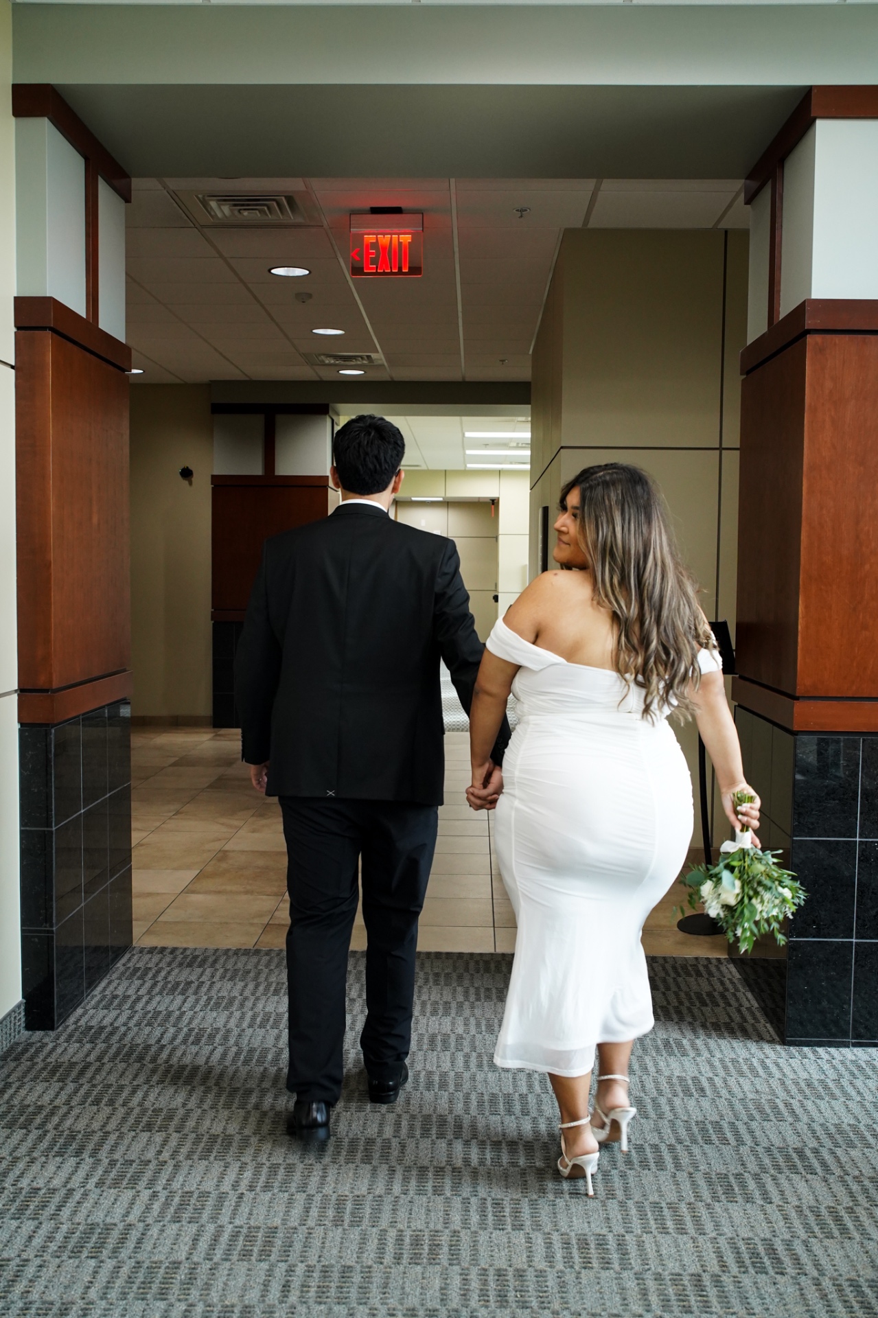 Bride and groom walking hand in hand toward the courthouse exit